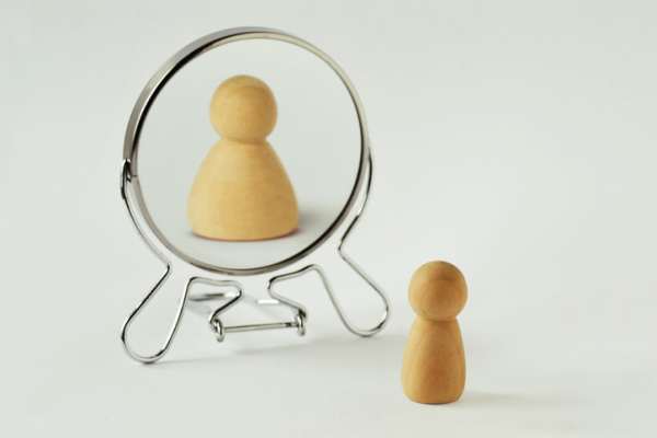 A small wooden pawn sees itself reflected in a round mirror in a distorted way as much heavier; concept of eating disorders